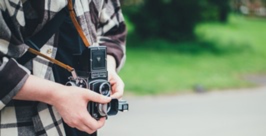 Someone in a park holding a camera near to his/her stomach and being ready to take a photo