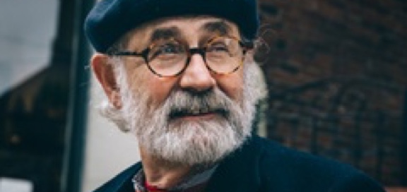 An old man with gray beard, glasses and a hat looking to the horizon