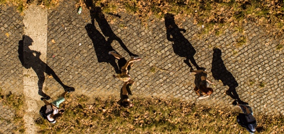 Top view of people walking left to right under the Sun and their shadow reflecting to the floor