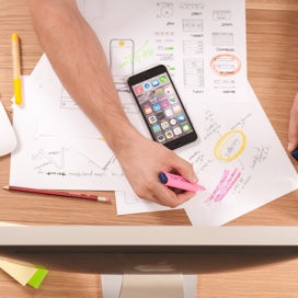 Someone writing o drawing ideas with marker on a white paper that is below his/her smartphone
